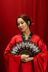 a girl in a red kimono with a black fan on a red background