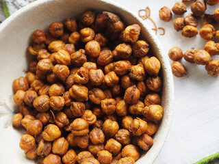 Garbanzos crujientes espaciados para tomar como snack, puestos en un bowl de cerámica rústica junto a sal y distintas especias, sobre un paño bordado y junto a rama de lavanda