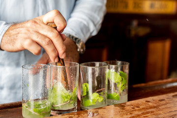 A skilled bartender expertly prepares a traditional Cuban mojito cocktail, complete with mint leaves and lime wedges.