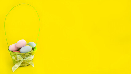 Wide Easter banner. Green basket with colorful eggs on a yellow background. Holiday concept, congratulation, postcard, template,copy space, text, mockup,spring,decoration,party,poster,design, religion