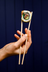 side view of one tasty Philadelphia roll in hand holding with bamboo chopsticks