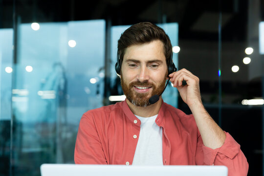 Mature successful businessman with video call headset working inside office, man consulting online clients, talking with colleagues on online remote meeting, sitting at workplace with laptop. - Powered by Adobe