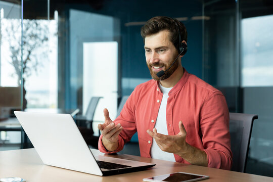 Mature successful businessman with video call headset working inside office, man consulting online clients, talking with colleagues on online remote meeting, sitting at workplace with laptop.