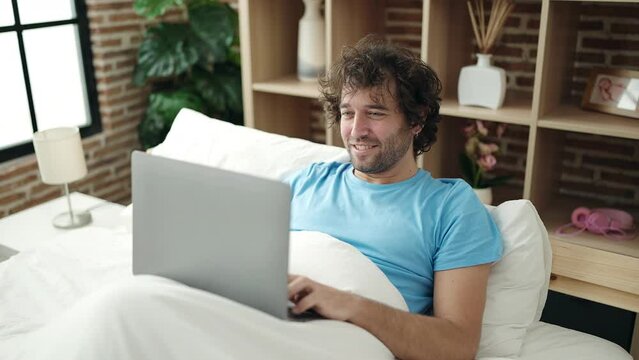 Young hispanic man using laptop lying on bed at bedroom