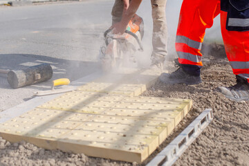 Builders cutting concrete tactile flags with a petrol power saw and placing them on concrete during pedestrian road crossing construction
