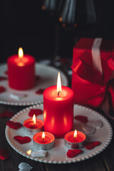 Saint Valentine's Day celebration. Red burning candles, hearts, gift box, postcard on dark wooden background. Happy holiday . Table decor for festive dinner, romantic atmosphere