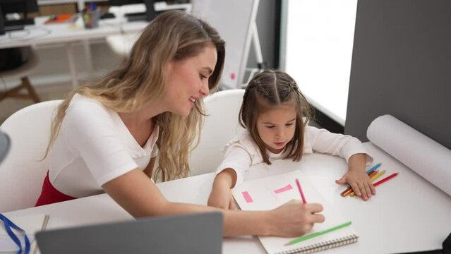 Teacher and toddler sitting on table drawing on notebook at classroom