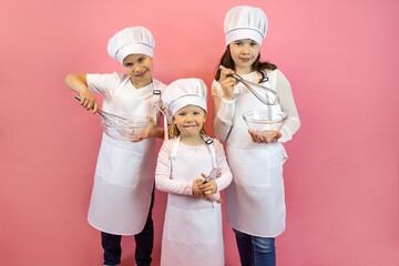 Happy chef kids in caps and apron, holding whisks and cups on a pink background. The concept of food, restaurant, training, poster, postcard, health, diet, nutrition,copy space, layout, hobby,job. 