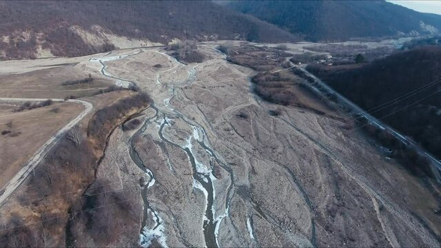 Dried up river bed in a rural countryside with the snowy mountains in the background. Majestic landscape with the rock road and hills.