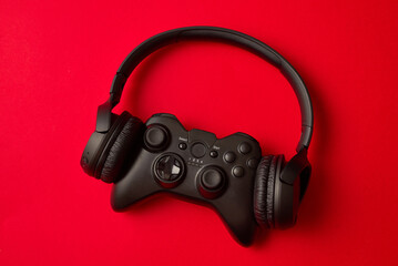 Black headphones and a gamepad on a red background. Concept of the game on the console or computer