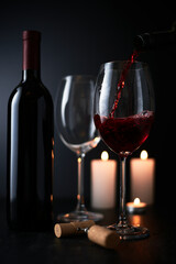 Pouring red wine into wine glass on dark background, still life background