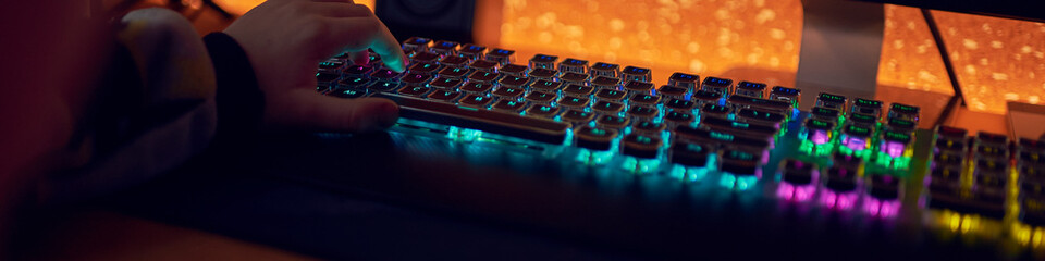 Hands of  gamer man playing video games on computer in dark room using backlit colorful keyboard © stenkovlad