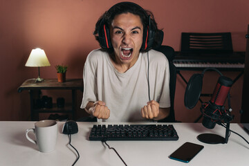 young gamer streamer guy with headset, microphone, gaming hardwareand a cup of coffee on the desk shouting celebrating euphorically looking at the camera