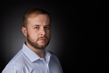 Young blond man with a beard, in a white shirt on a dark background.