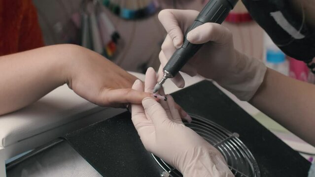 close up women hands. Manicurist using milling cutter manicure to remove gel or acrylic from customer fingernails. Nail salon, professional, beauty concept.