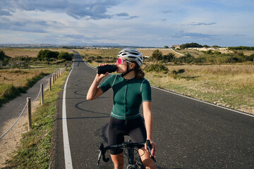 Female cyclist a gravel bike drinks water during exercise.Empty city road.
Sports motivation.Murcia...