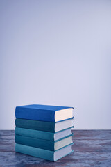 A stack of several books in fabric textured covers in beautiful emerald and blue colors on an old wooden table against a light background. Copy space view. Education, book publishing, love of reading
