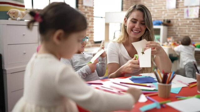 Teacher with boy and girl sitting on table having handcrafts class at kindergarten