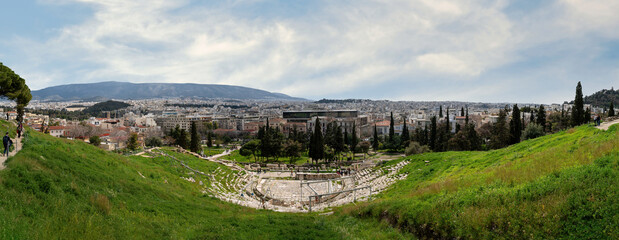 The ancient greek Theater of Dionysus (or Dionysos) is built on the south slope of the Acropolis hill. Panoramic view to the Attica basin, sunny day, cloudy blue sky