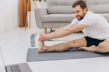 Handsome bearded man doing hamstring stretch exercise at home.