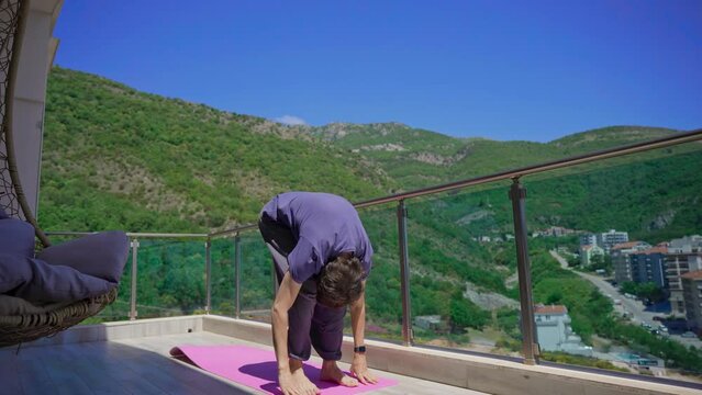 Young man is practicing yoga on in modern apartment terace with mountains and sea in the background