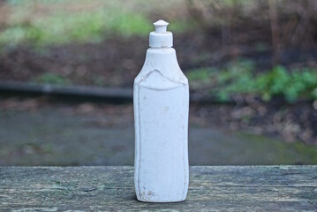 one large closed dirty old gray white plastic bottle stands on a wooden table in the street