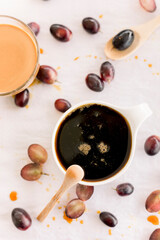 Jar of grape molasses, grape syrup. Sweetener, cough medicine. Black, green and purple grapes on kitchen table.