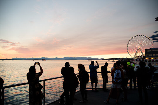 Silhouetted tourists taking photos at the waterfront at sunset with Ferris Wheel.