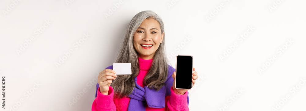 Wall mural online shopping. closeup of smiling asian senior woman showing blank mobile screen and plastic credi