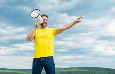 man in yellow shirt shout in megaphone on sky background. point finger