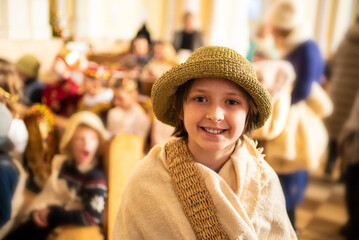 A child dressed as a Shepherd stands near children dressed as angels and shepherds in the temple. children are preparing for a Christmas performance in a Catholic church
