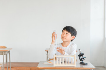 Fototapeta na wymiar 学校の授業で理科の実験・観察・研究・勉強をする小学生の男の子(顕微鏡・試験管・スポイト) 