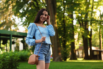 Fototapeta premium Beautiful young woman with stylish bag at park outdoors, space for text