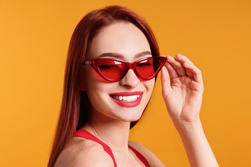 Fototapeta premium Happy woman with red dyed hair and sunglasses on orange background