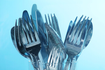 Washing silver cutlery in water on light blue background