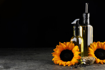 Sunflower cooking oil, seeds and beautiful flowers on grey table against black background. Space...
