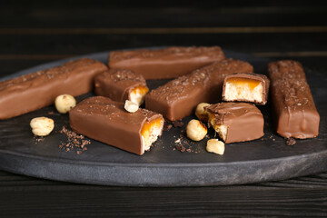 Board with delicious chocolate bars and nuts on black wooden table, closeup