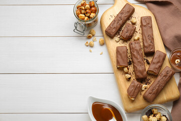 Board with delicious chocolate bars, caramel and nuts on white wooden table, flat lay. Space for text