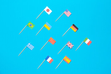 Many small paper flags of different countries on light blue background, flat lay