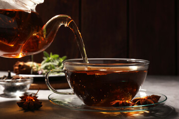 Pouring aromatic anise tea from teapot into glass cup on light grey table