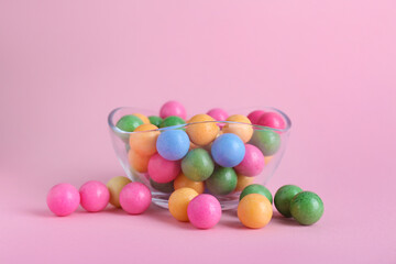 Bowl with many bright gumballs on pink background