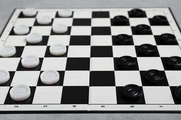 Checkerboard with game pieces on light grey table, closeup