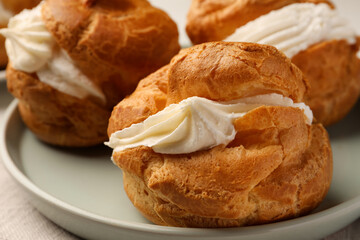 Delicious profiteroles with cream filling on plate, closeup