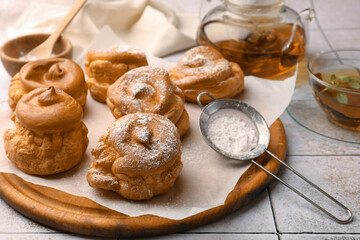 Delicious profiteroles with powdered sugar and tea on white tiled table