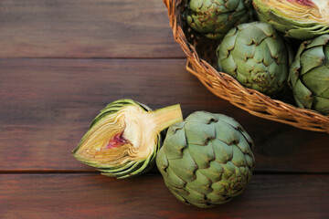 Wicker basket with fresh raw artichokes on wooden table