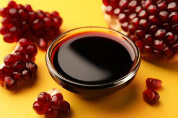 Glass bowl of tasty pomegranate sauce and fresh ripe fruit on yellow background, closeup