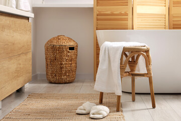 Fototapeta na wymiar Wicker stool with towel and slippers on rug in bathroom