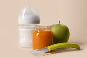 Healthy baby food in jar, bottle of milk, apple and spoon on beige background