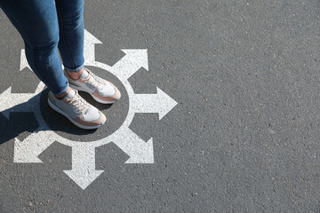 Choice of way. Woman standing in drawn circle with marks on road, closeup. White arrows pointing in...