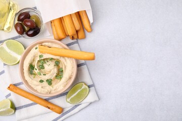 Fototapeta na wymiar Delicious hummus with grissini sticks served on light grey table, flat lay. Space for text